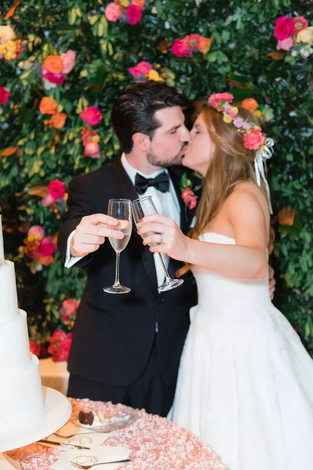 bride and groom champagne flutes kissing with floral wall behind at avon theatre