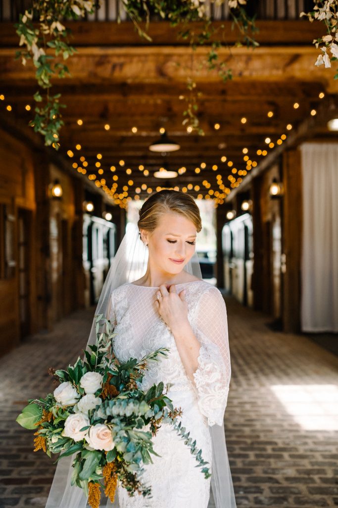 bride posing in wedding dress with bouquet inside at swan lake stables