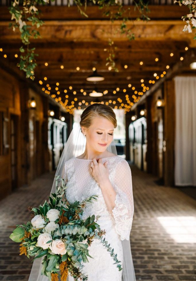 bride posing in wedding dress with bouquet inside at swan lake stables